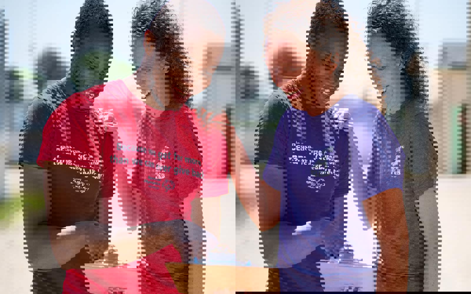 Une personne portant une chemise rouge avec les mots « Parce que nous recevons bien plus que nous ne pourrons jamais donner en retour » tient et montre un bloc-notes tandis qu'une personne portant une chemise violette sourit en regardant le bloc-notes.