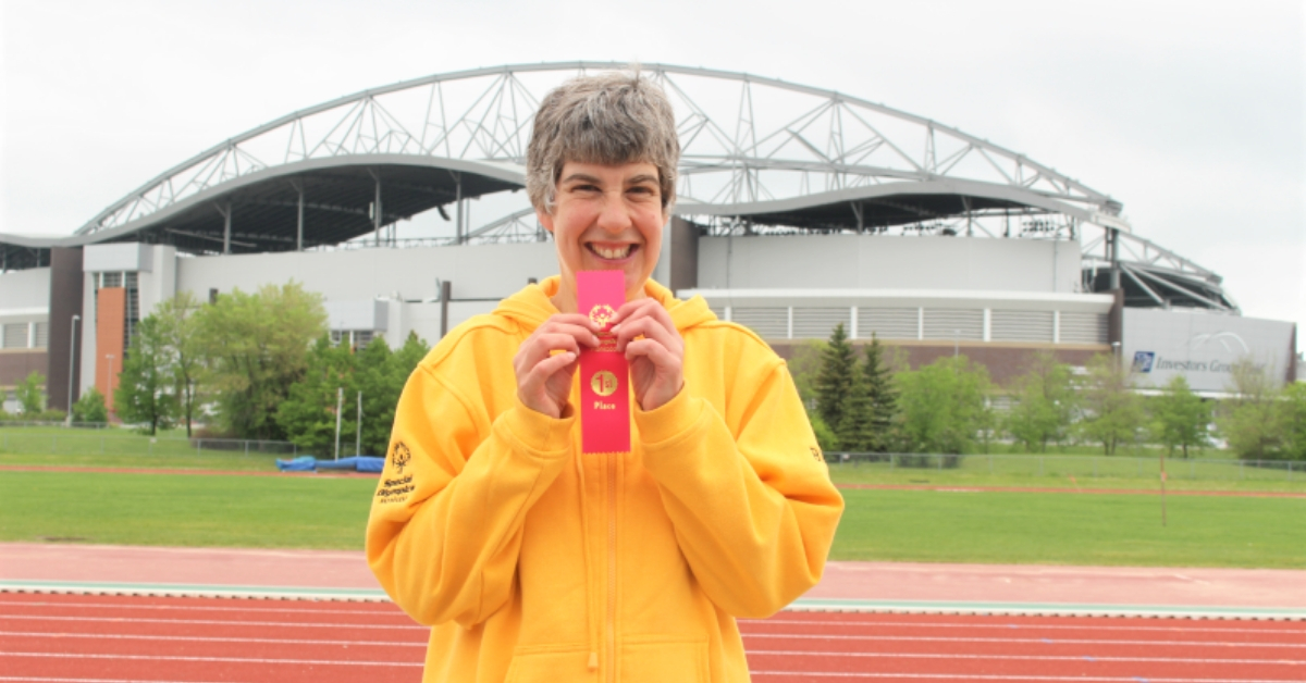Special Olympics Manitoba athlete Brita Hall stands on a track holding up a first place ribbon.
