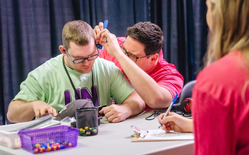 a male volunteer does an exam on a male athletes ears. 