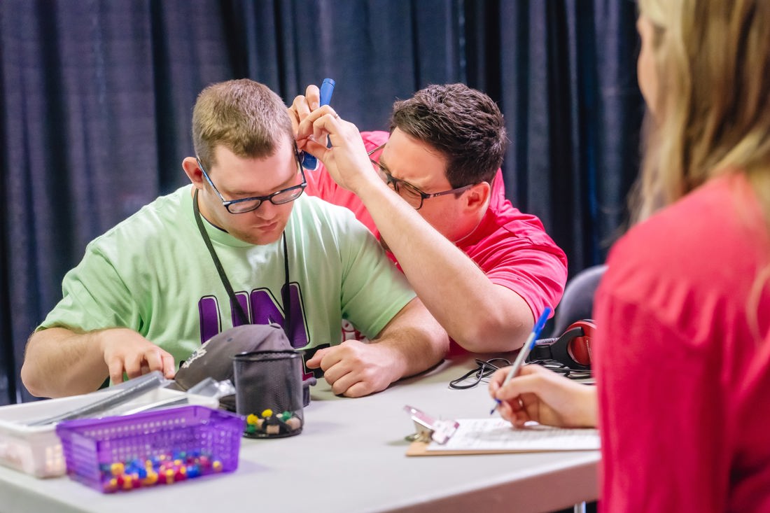 a male volunteer does an exam on a male athletes ears. 