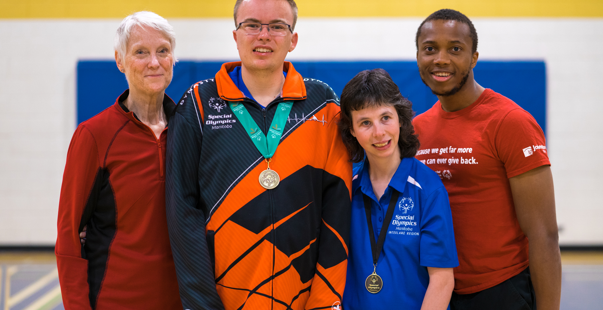 Quatre adultes debout ensemble, souriant à la caméra. Tous sont vêtus d'une tenue de sport. Deux d'entre eux ont des médailles autour du cou.