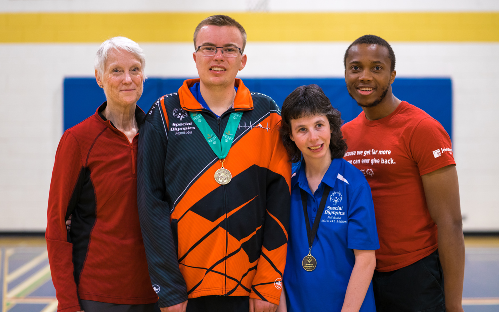 Quatre adultes debout ensemble, souriant à la caméra. Tous sont vêtus d'une tenue de sport. Deux d'entre eux ont des médailles autour du cou.