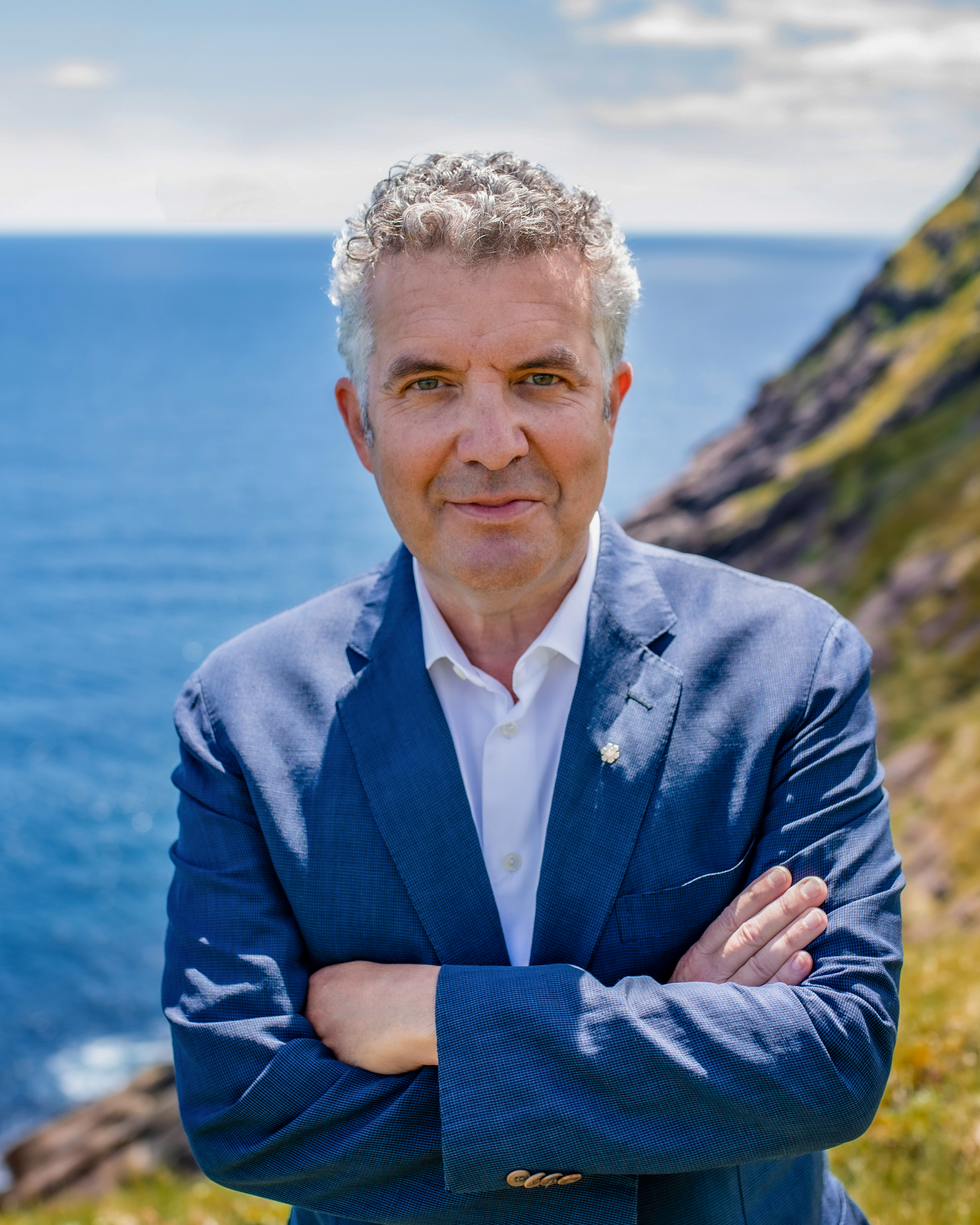 Man in a blue blazer with his arms crossed. Behind him is the ocean. Man in a blue blazer with his arms crossed. Behind him is the ocean.
