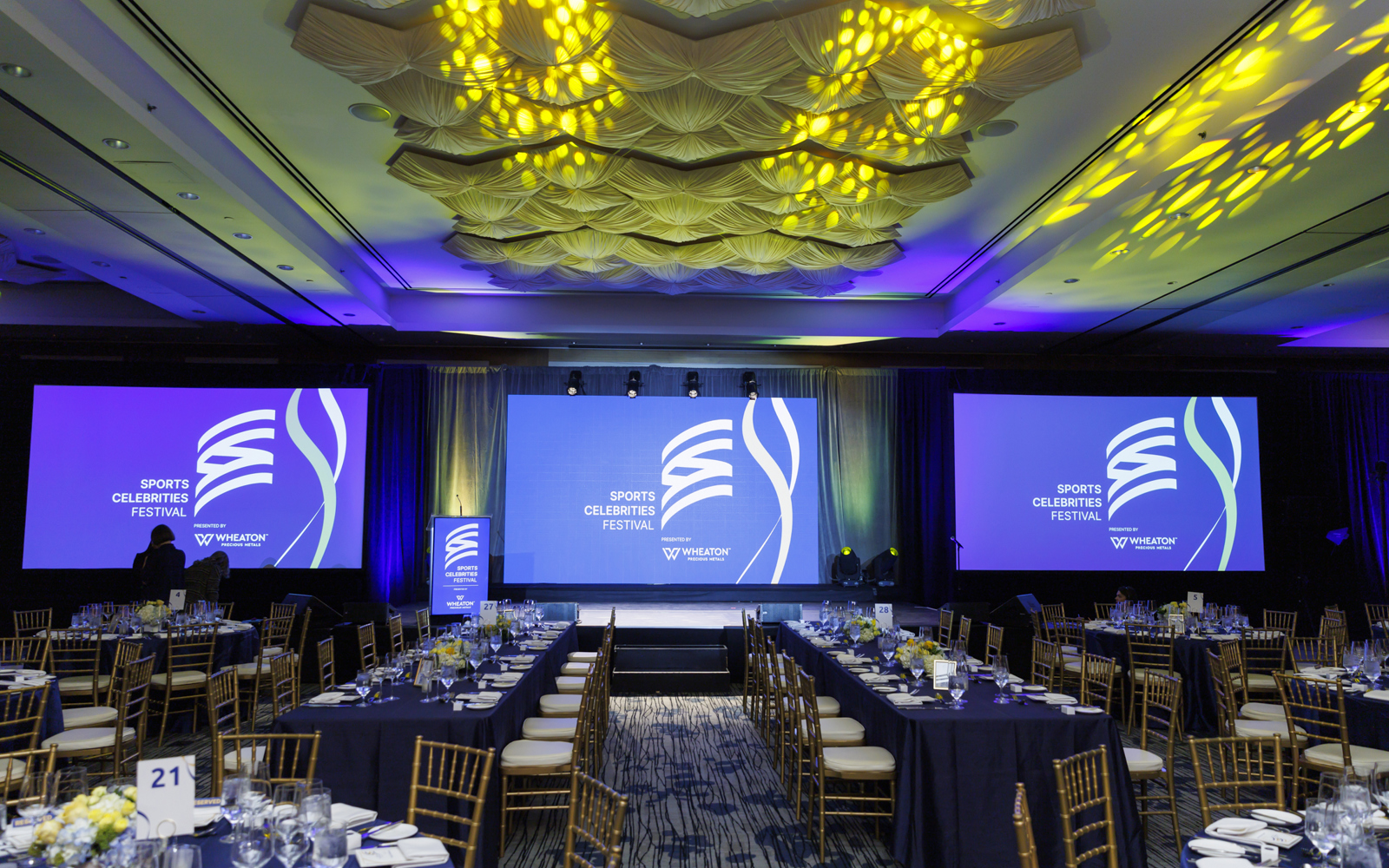 The Sport Celebrities Festival room before guests arrive shows tables set, large screens brightly showing the event logo.