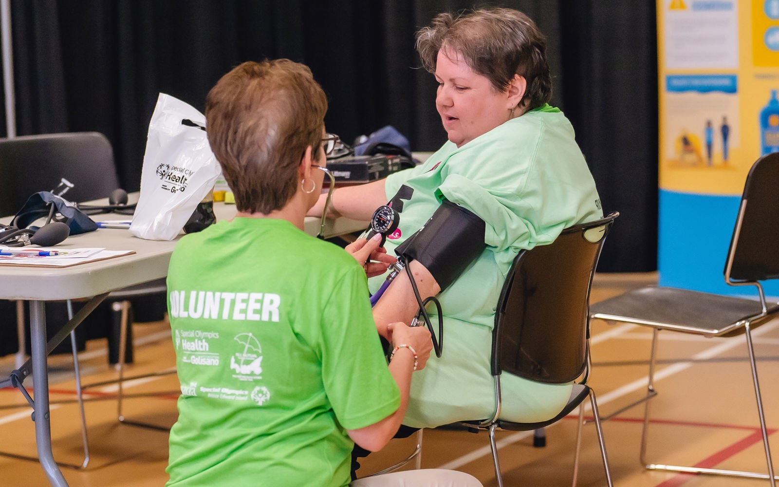 a person in a green tshirt takes the blood pressure of another person in a green tshirt.