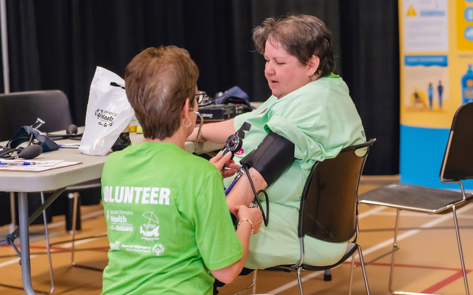 a person in a green tshirt takes the blood pressure of another person in a green tshirt. 