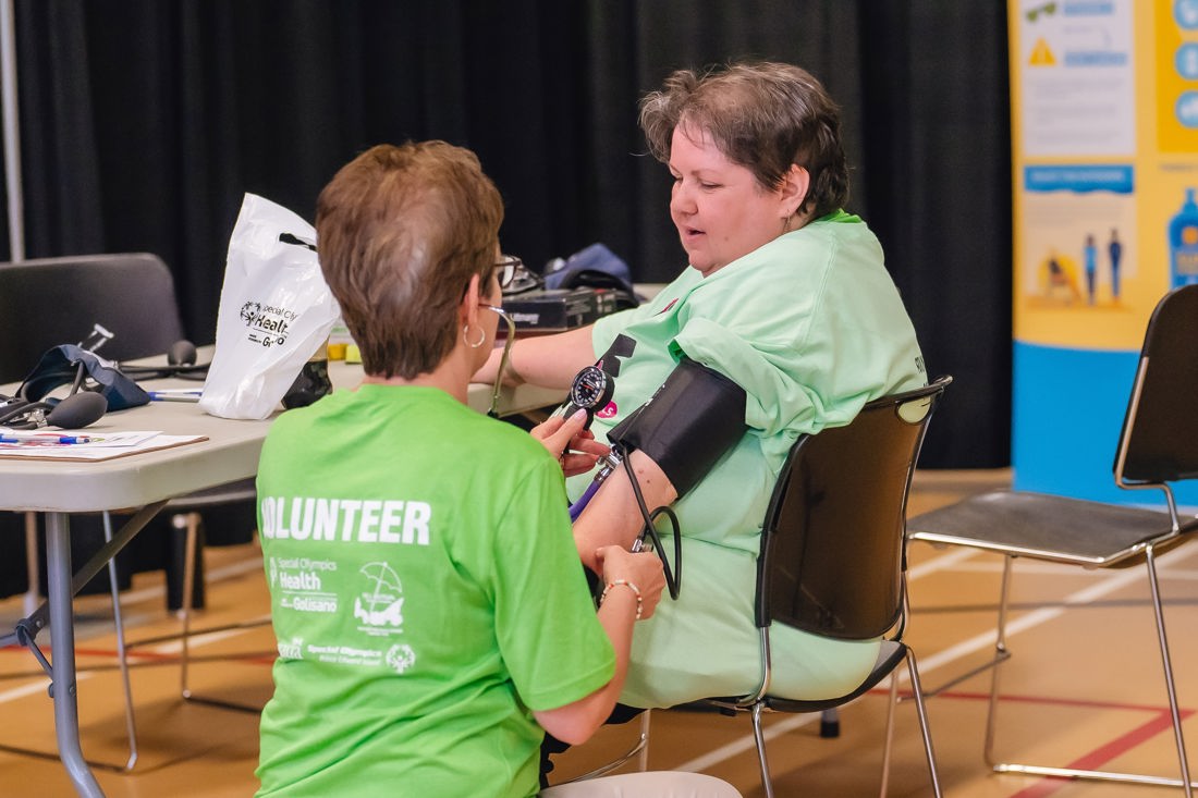 a person in a green tshirt takes the blood pressure of another person in a green tshirt. 