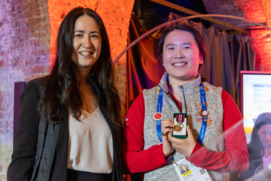 Two women stand beside each other smiling at the camera. 