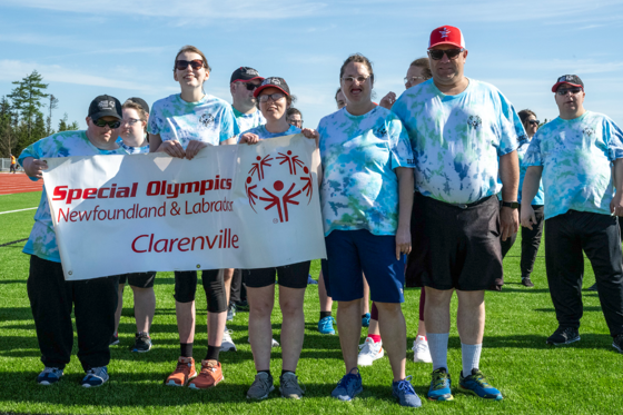 A group photo of the Clarenville Allstars Community Club. Everyone in the photo is wearing a blue tie-dye shirt. Three athletes are holding up a banner that says "Special Olympics Newfoundland & Labrador Clarenville".