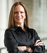 Woman with long hair and wearing a black shirt,with her arms crossed, looking at the camera. 