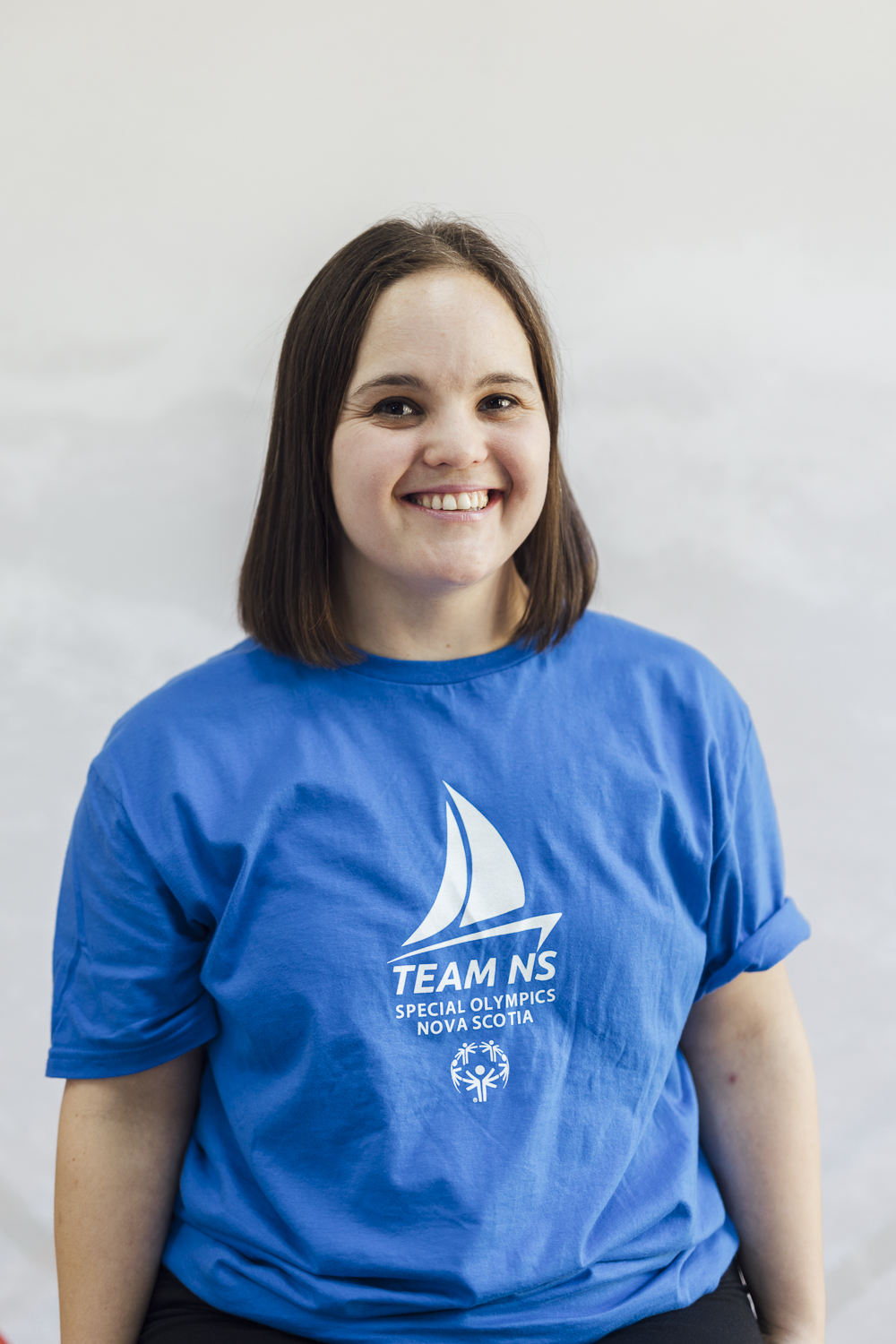 Young woman with dark hair and a blue tshirt smiles at the camera