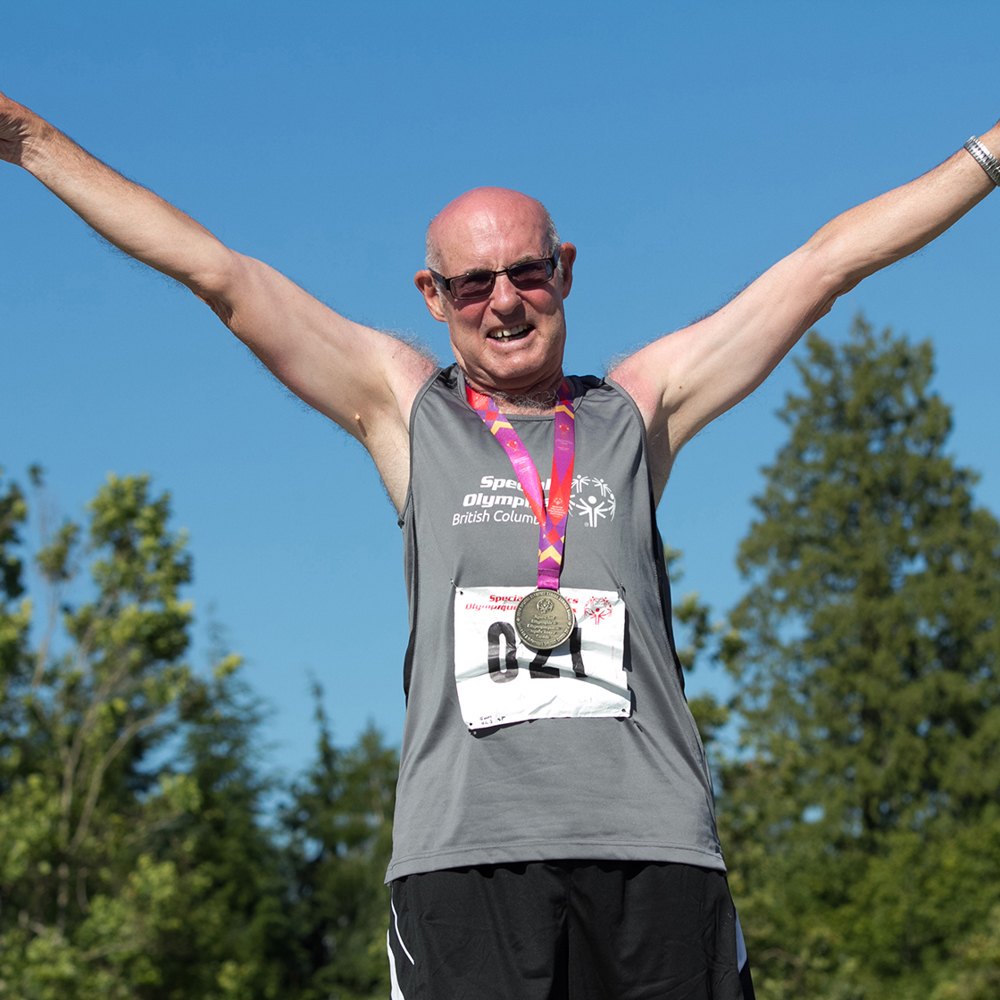 Special Olympics BC athlete celebrates his podium finish with arms raised and a big smile at the 2014 Special Olympics Canada Games.