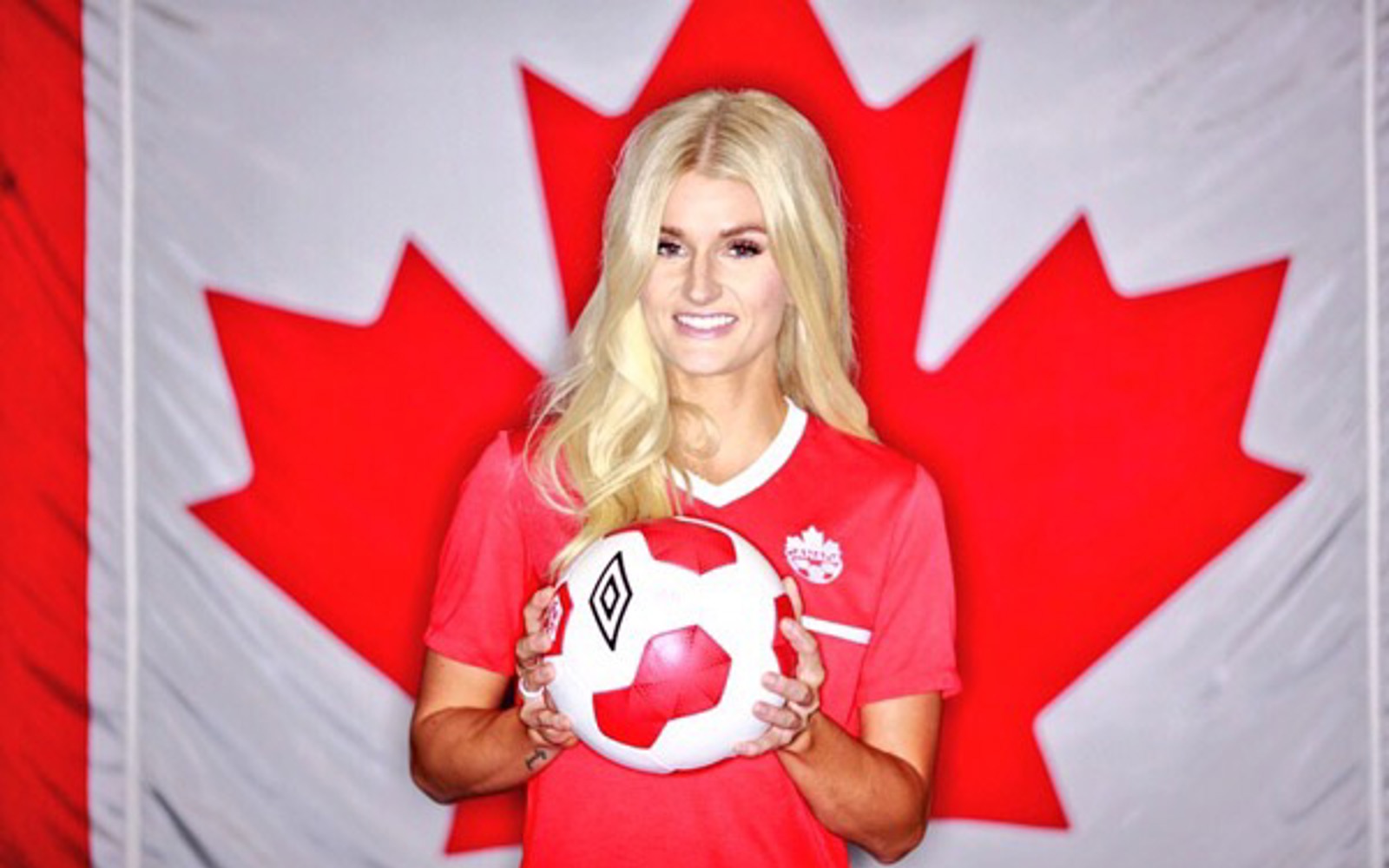 Portrait d'une femme aux longs cheveux blonds devant un drapeau canadien, tenant un ballon de football.