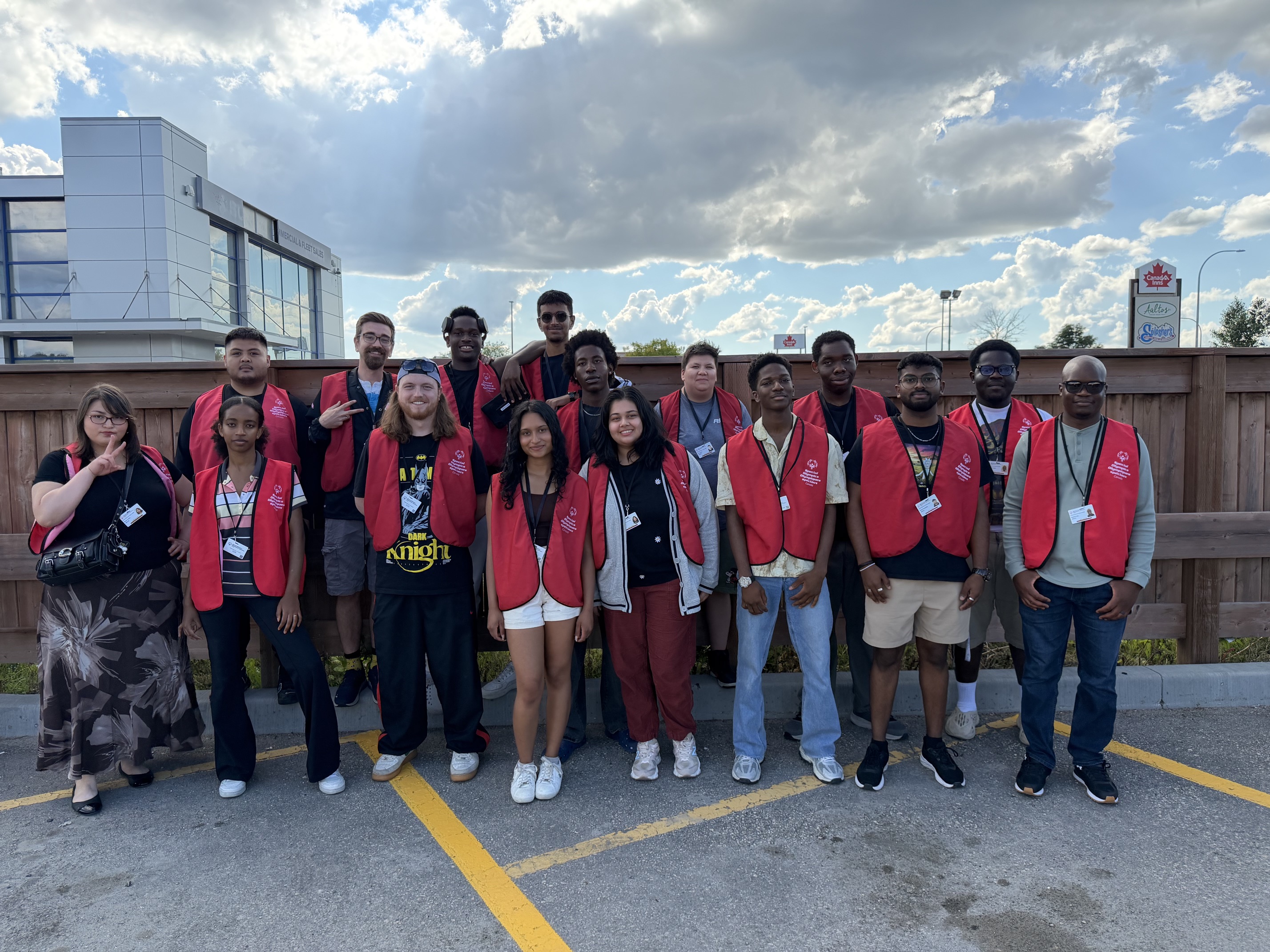 A group of 16 face to face canvassers pose together, smiling at the camera. The are all wearing red Special Olympics Canada branded vests. 