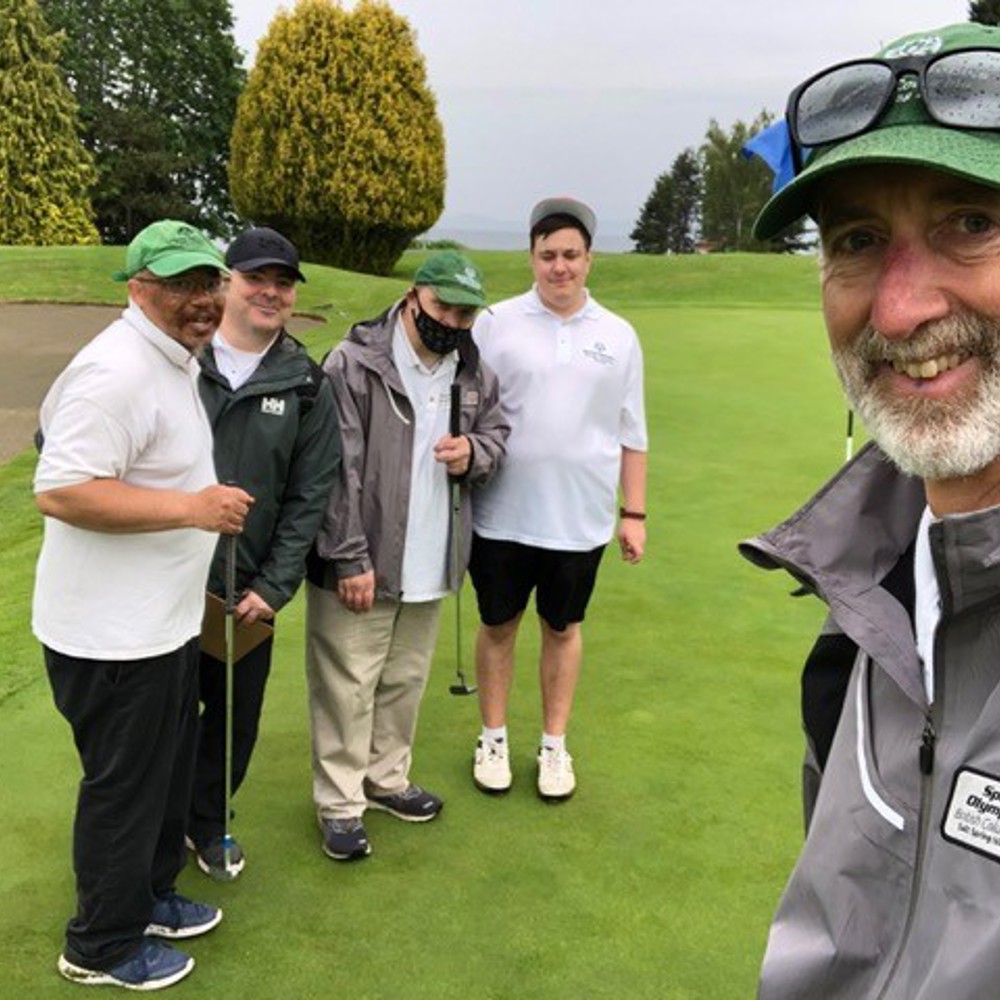 A group of four golfers are on the green posing for a photo with their coach.