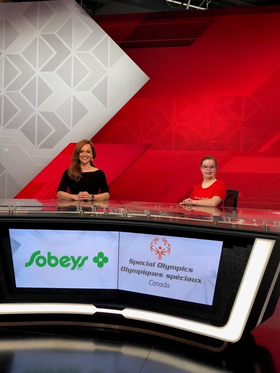 Deux femmes sont assises derrière un bureau, devant un écran sur lequel figurent les logos de Sobeys et des Olympiques spéciaux Canada. 