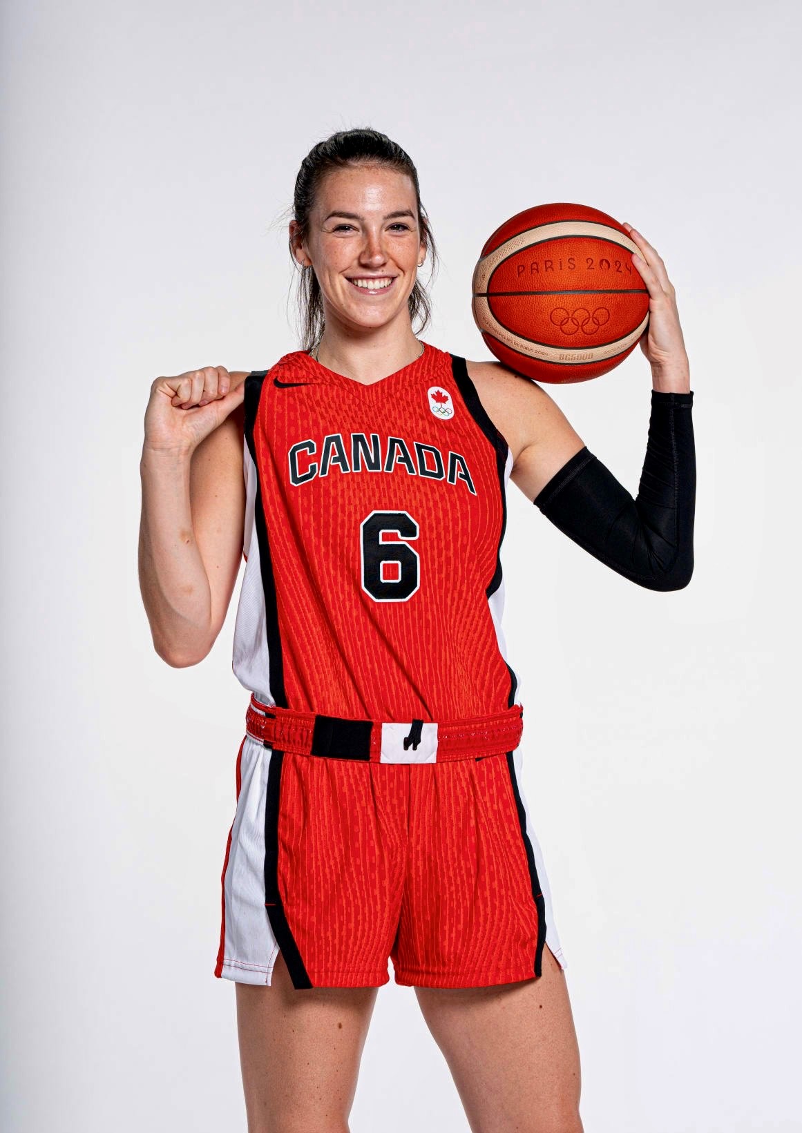 Woman in a red Team Canada basketball uniform holding a basketball that says Paris 2024 Woman in a red Team Canada basketball uniform holding a basketball that says Paris 2024
