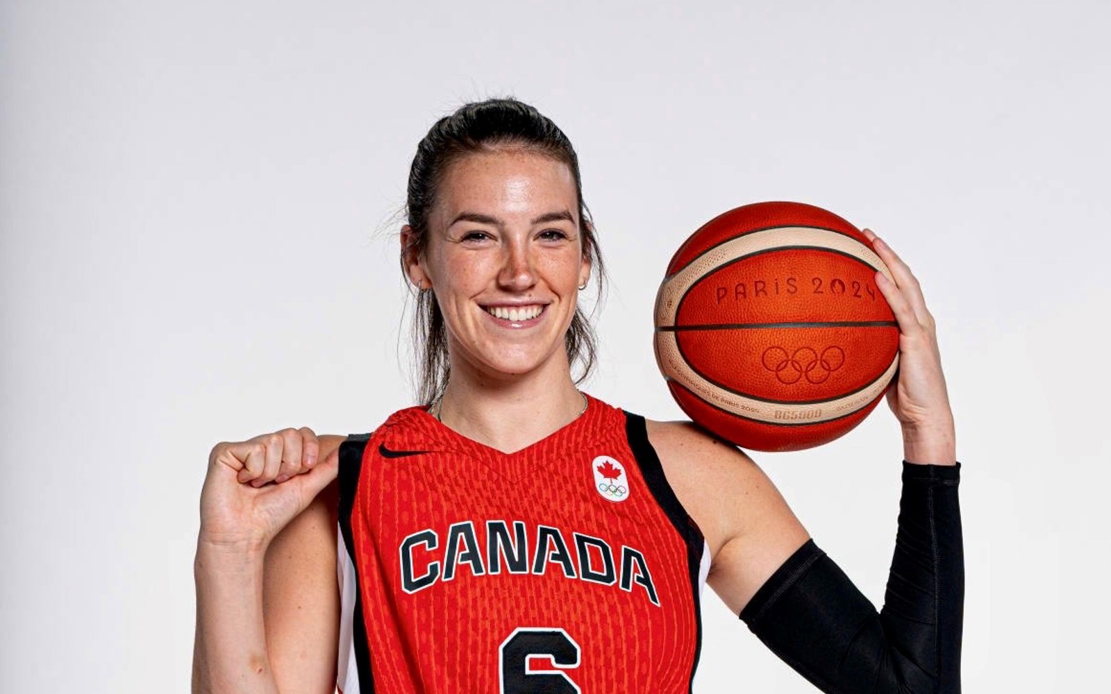 Femme vêtue d'un maillot de basket-ball rouge de l'équipe canadienne, tenant un ballon de basket sur lequel est inscrit « Paris 2024 ».