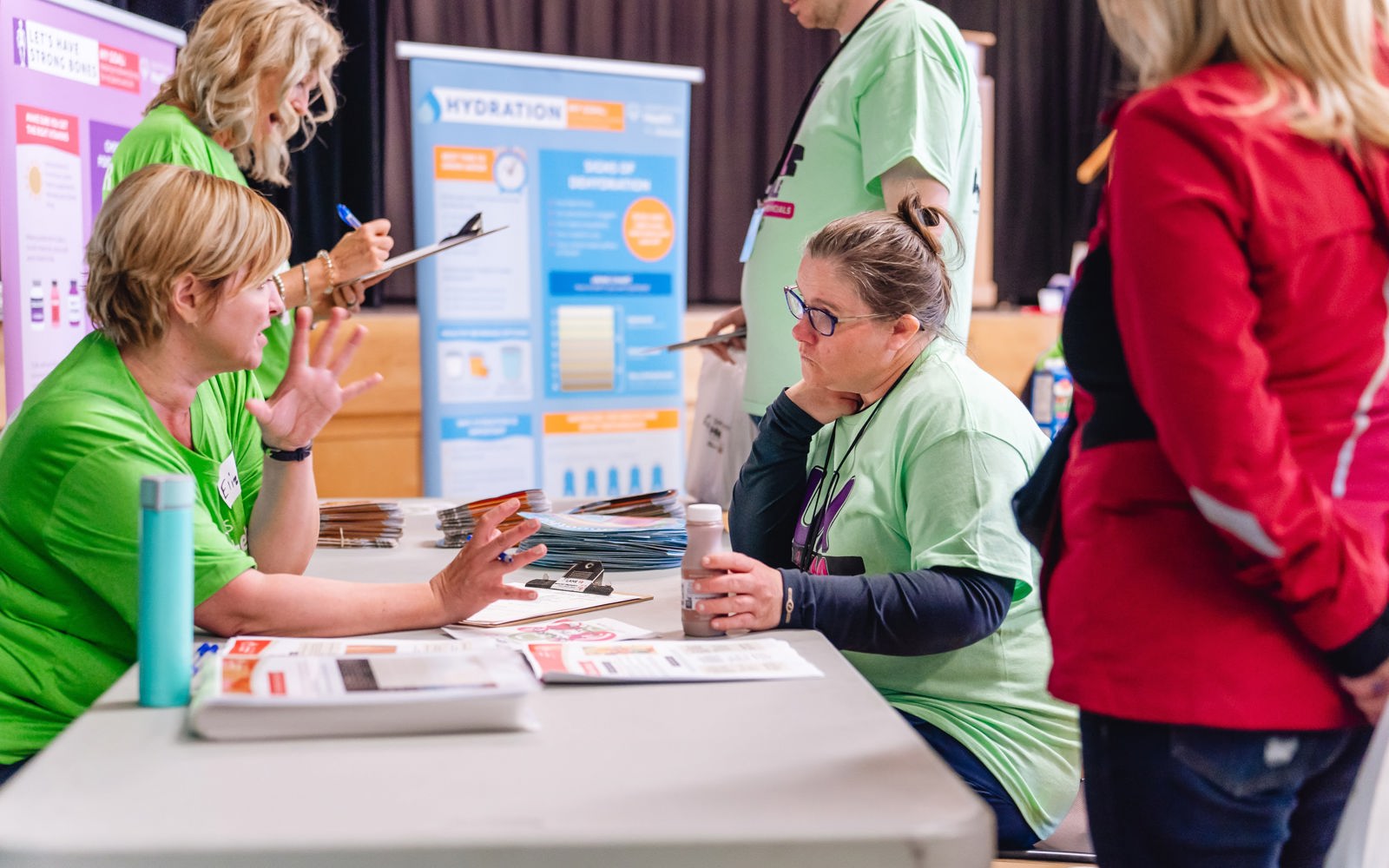 Woman in a green tshirt shares information with a woman sitting across from her. 