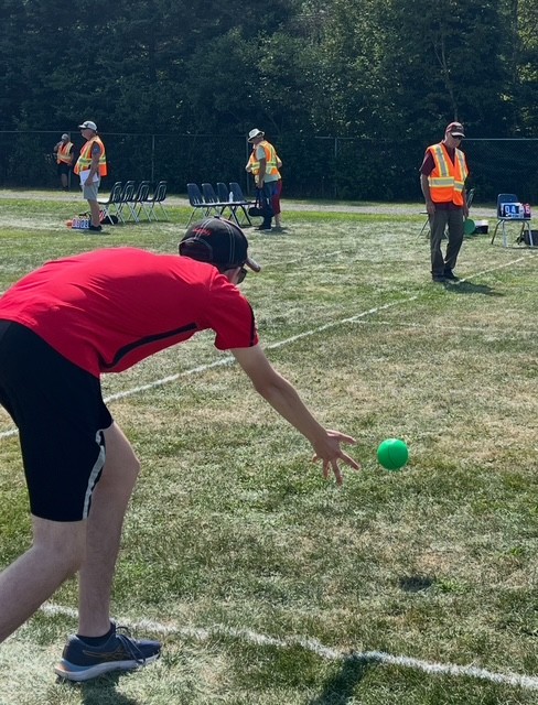 Man in black shorts and red shirt throwing a bocce ball on green grass Man in black shorts and red shirt throwing a bocce ball on green grass