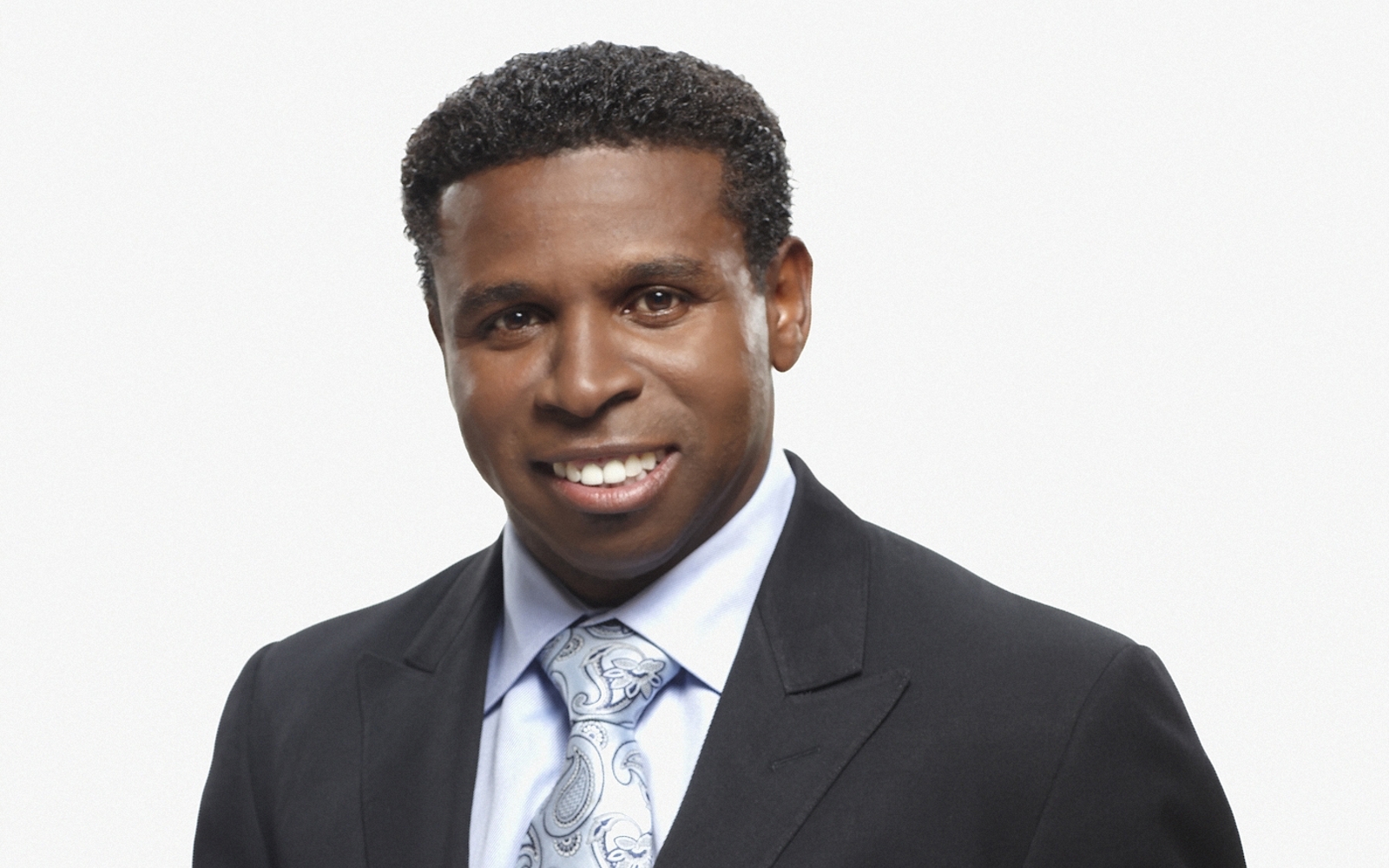 Portrait d'un homme en costume noir et cravate bleue et blanche à motif cachemire.