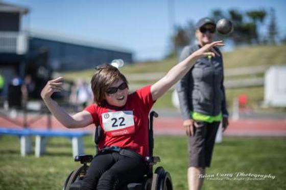 Person in a wheelchair with a red shirt and a number tag throwing a shot put 