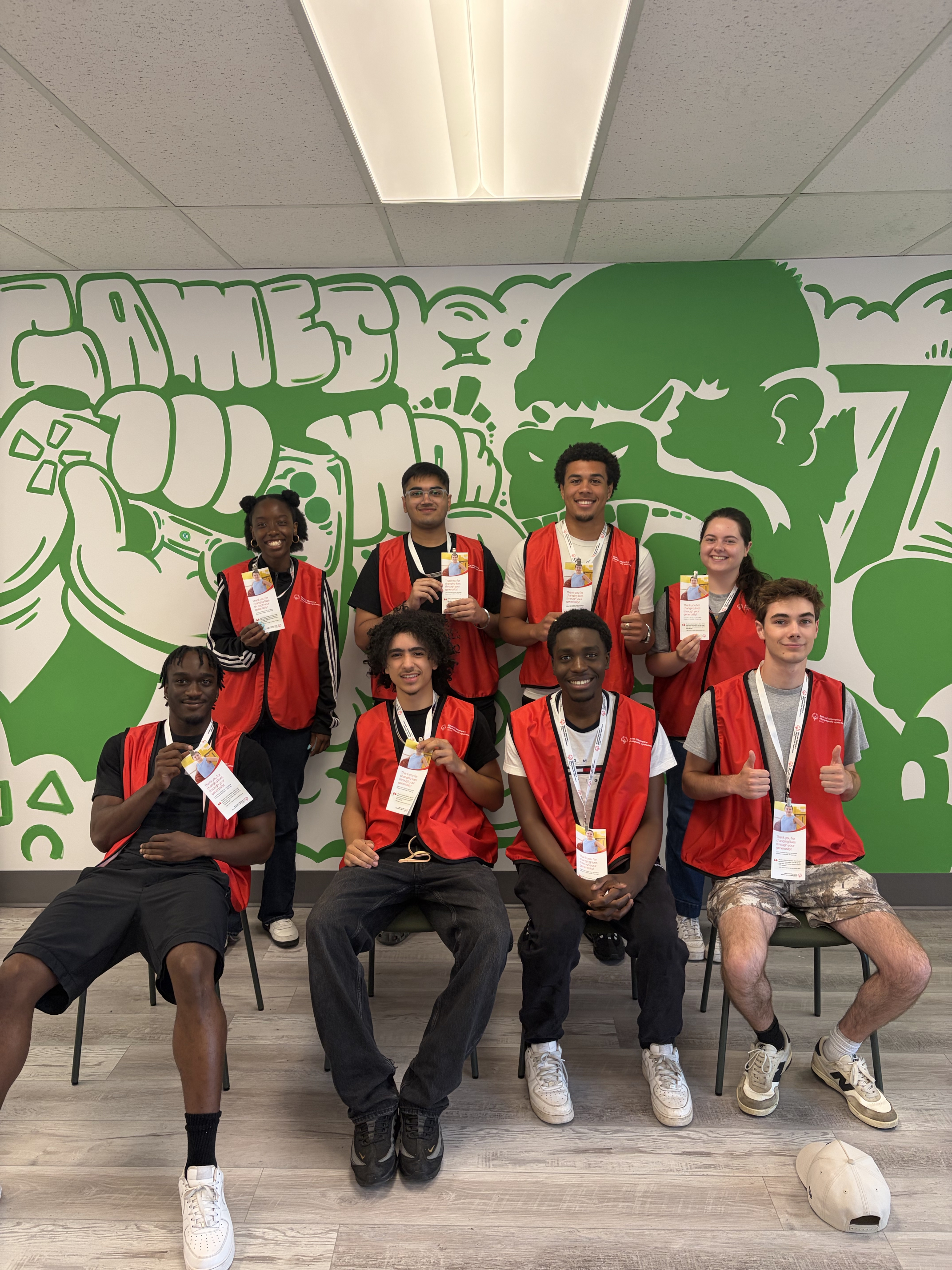 A group of 8 face to face canvassers pose together, smiling at the camera. The are all wearing red Special Olympics Canada branded vests. 