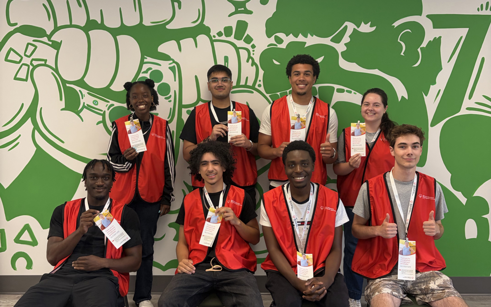Un groupe de huit solliciteurs en personne pose ensemble, souriant à la caméra. Ils portent tous des gilets rouges portant le logo de Special Olympics Canada. 