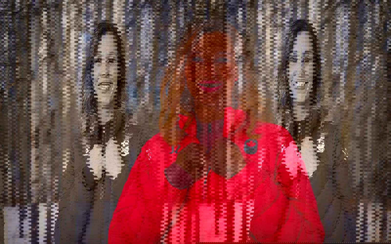 Gros plan sur une femme à l'extérieur en hiver dans une forêt, vêtue d'une veste rouge aux couleurs des Jeux Olympiques.