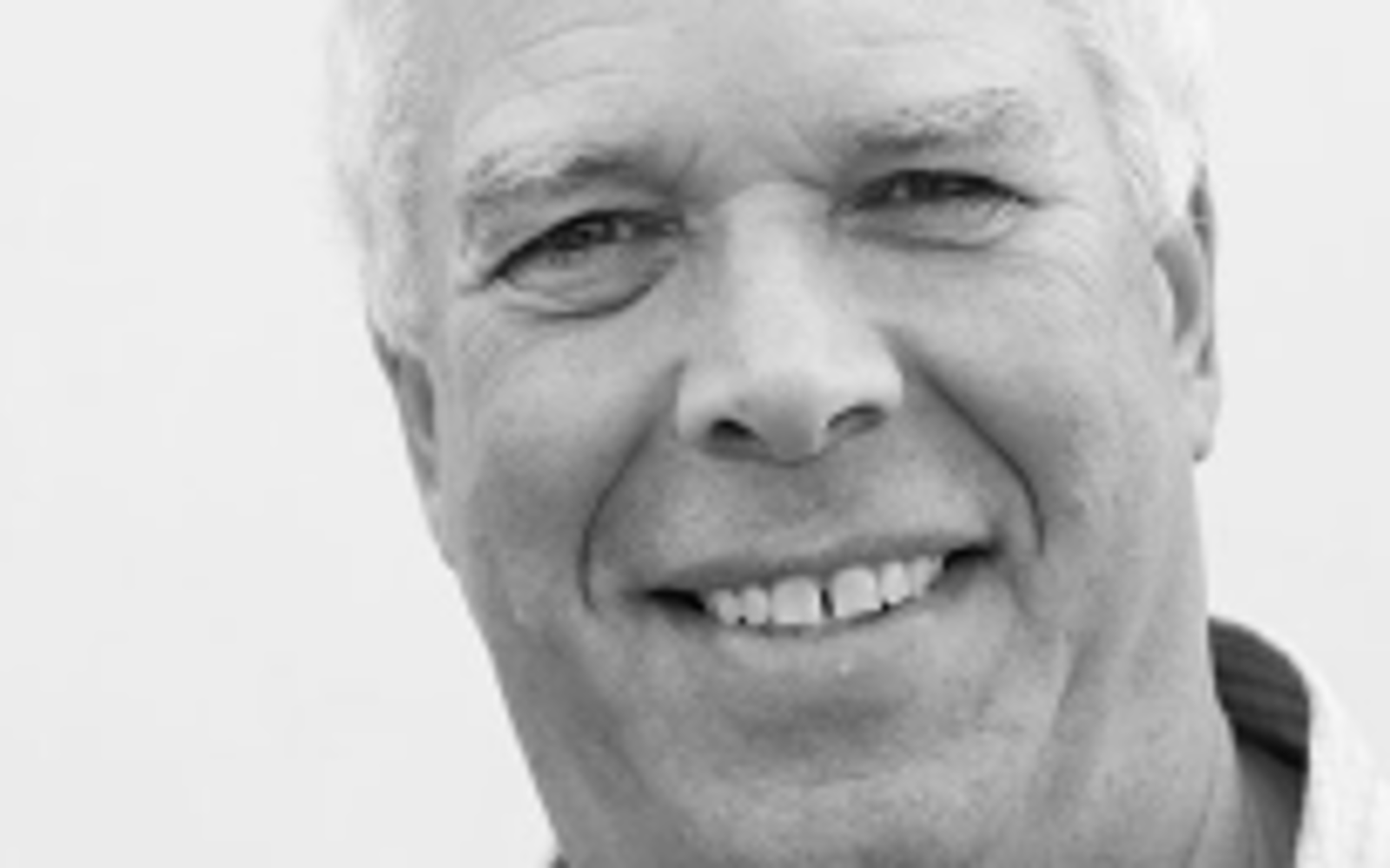 Black and white photo of a man smiling at the camera.