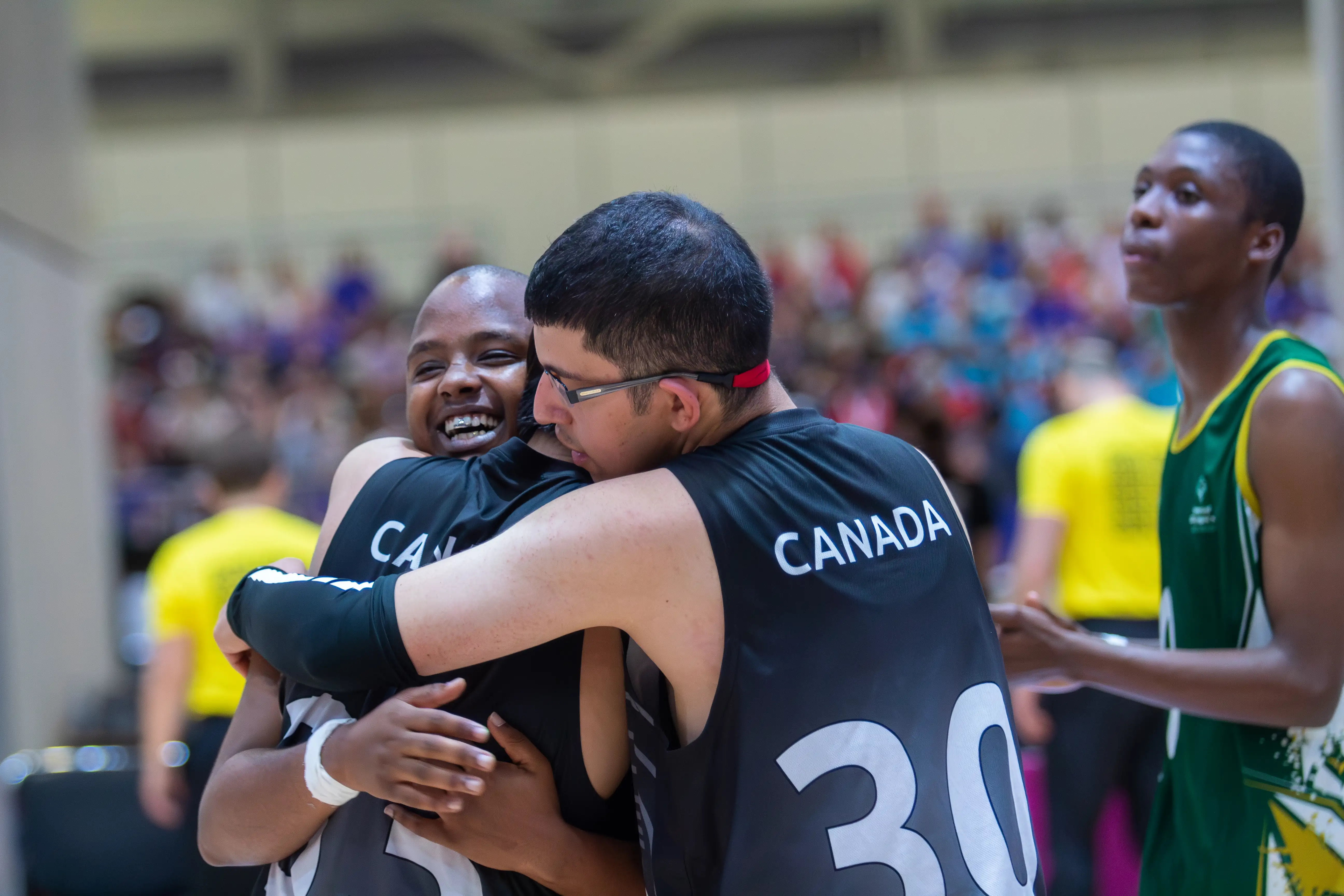 Three athletes engaging in a group hug. For two of the athletes we can only see their backs and they are wearing black 
