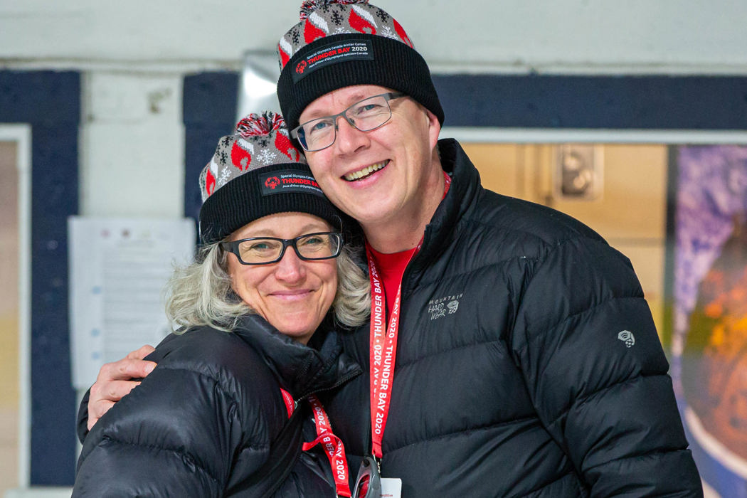 Deux personnes vêtues de vestes d'hiver noires et coiffées de tuques Thunder Bay 2020 sourient à la caméra. 