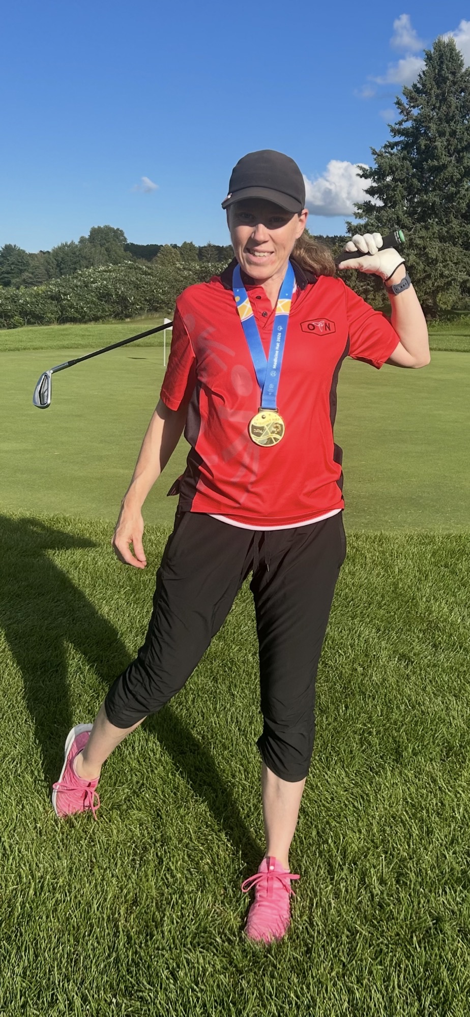 Catherine Partlow posing with a golf club, in Special Olympics Ontario attire and a gold medal around her neck. 
