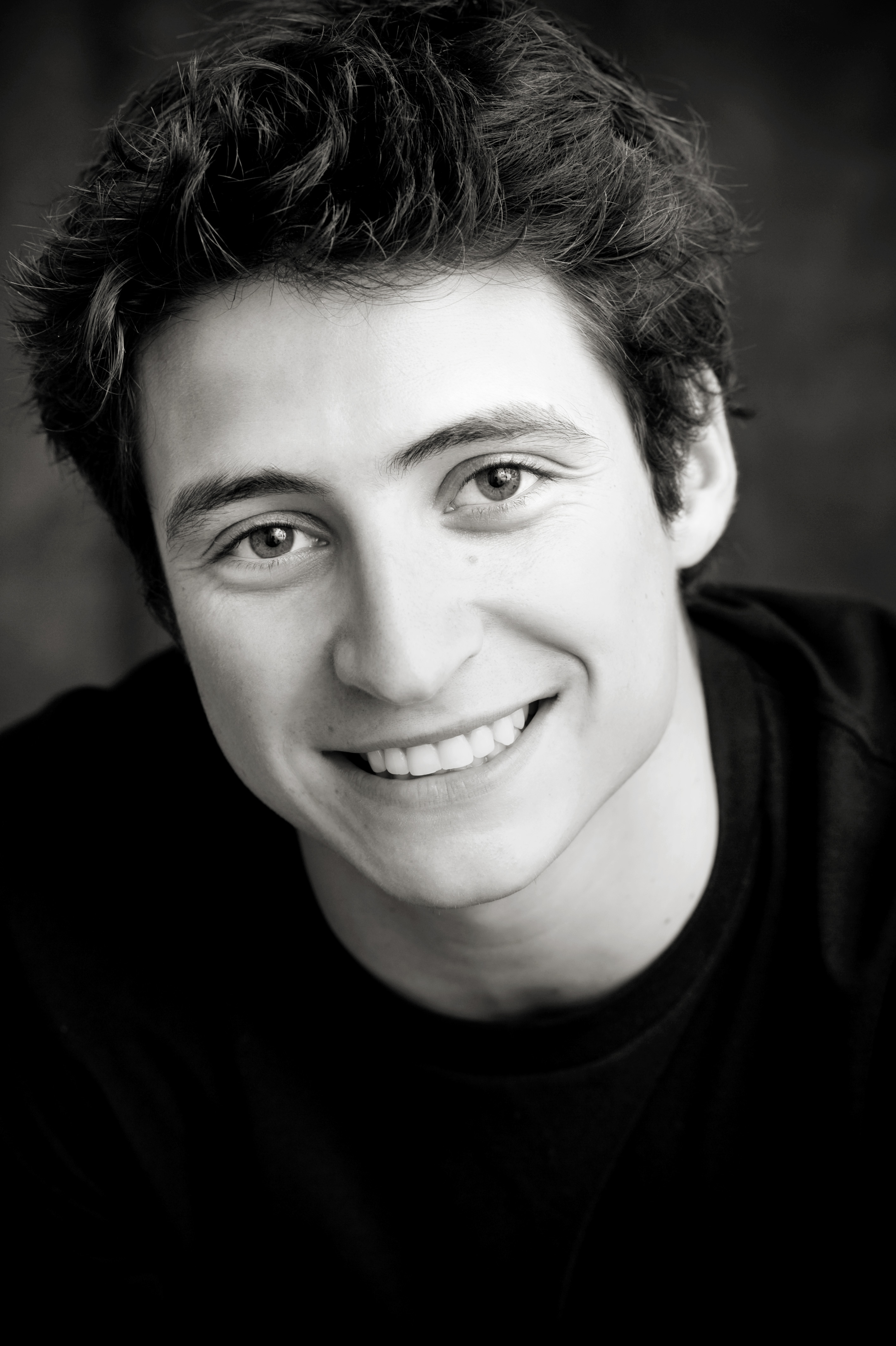 Black and white headshot of a man with dark hair and black shirt. Black and white headshot of a man with dark hair and black shirt.
