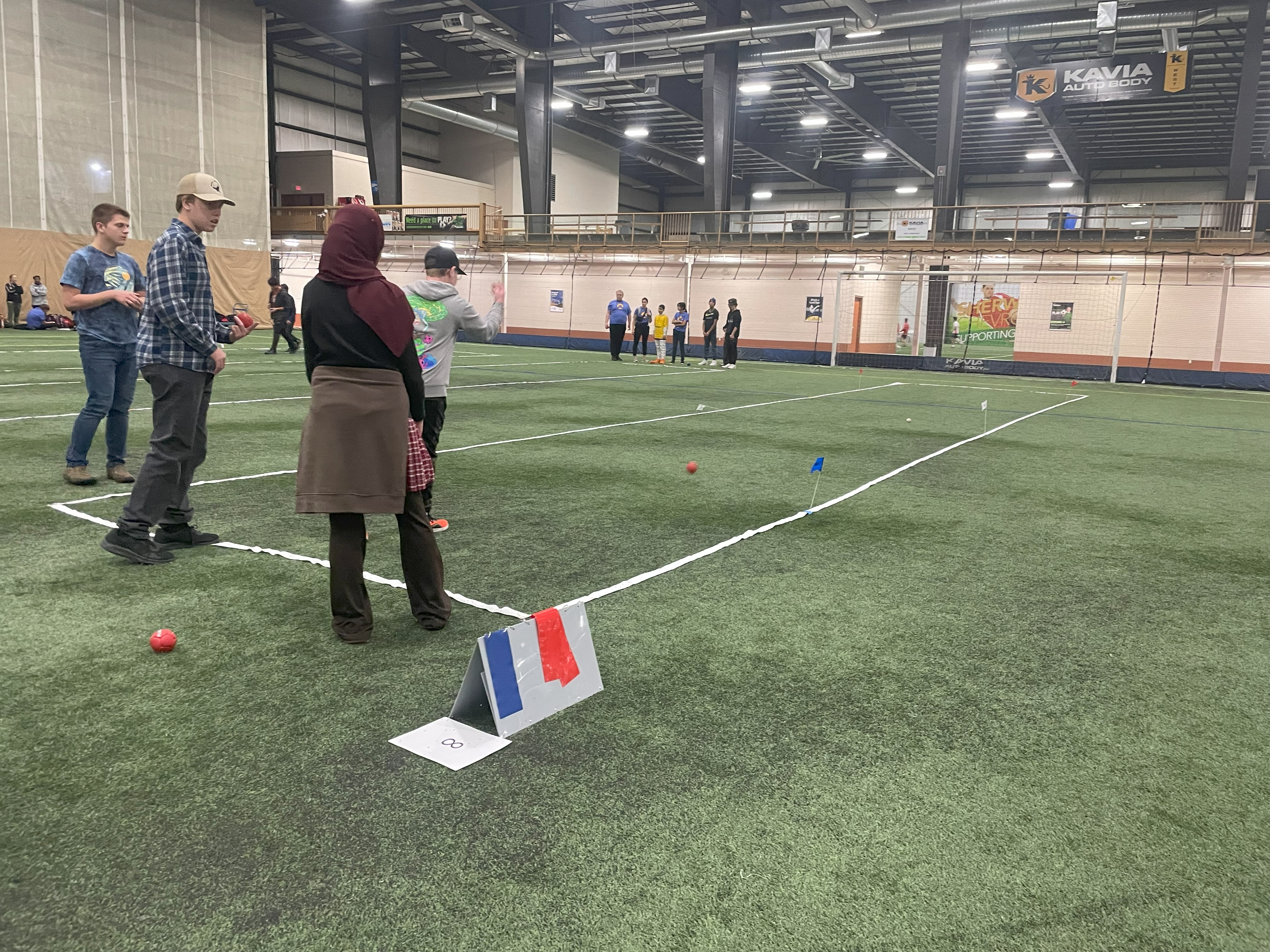 A unified sports match. Wide shot image of athletes playing bocce on a field. Four athletes are seen playing closer to the camera, while another group of athletes can be seen playing in the distance.
