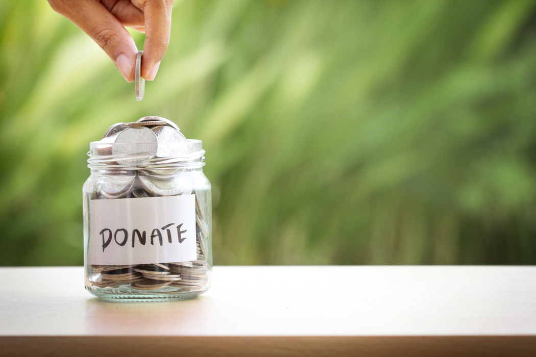 Hand putting money in a jar. Jar says donate on it. 