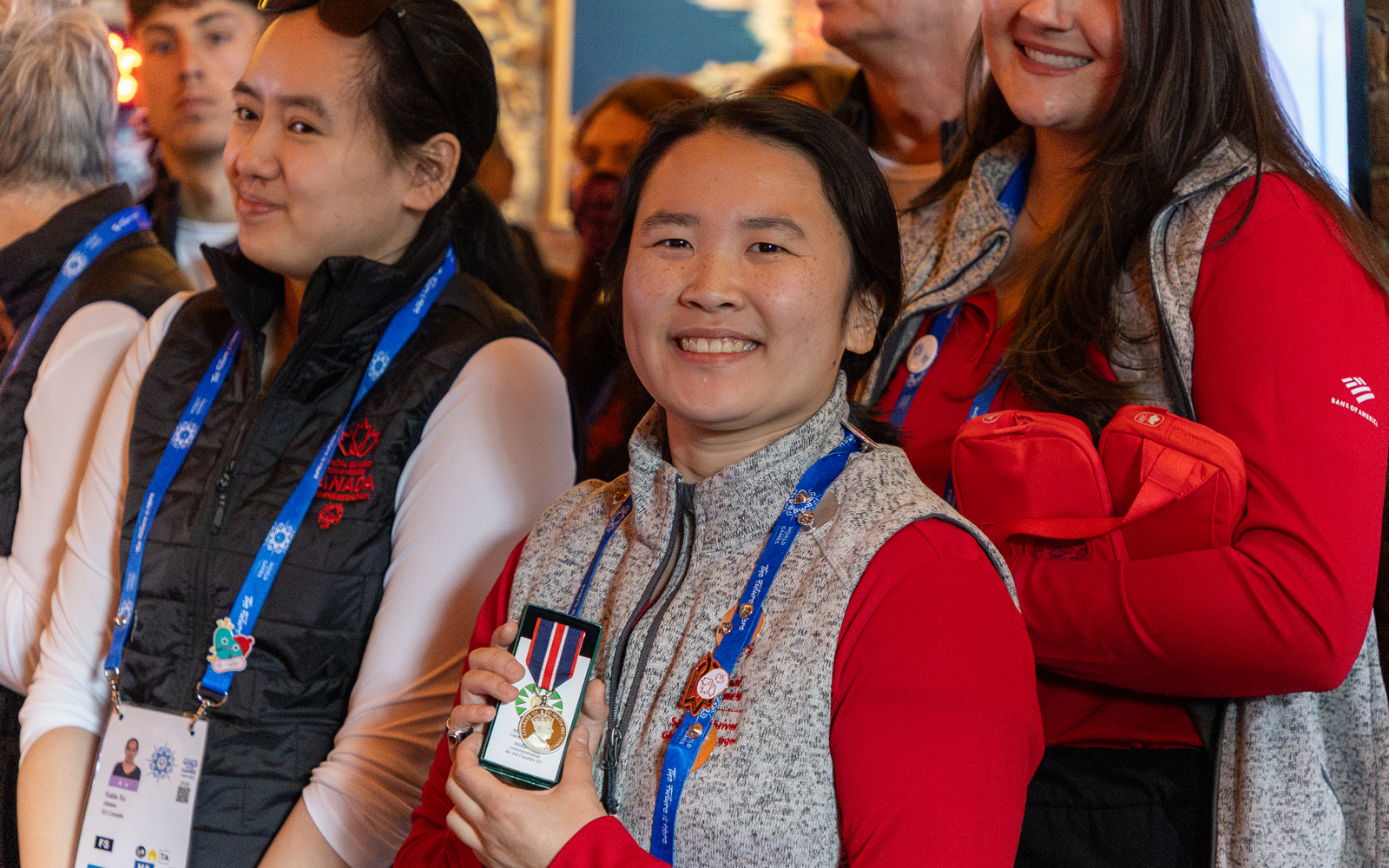 Two girls standing beside each other, One is looking at the camera smiling and holding up a medal. 