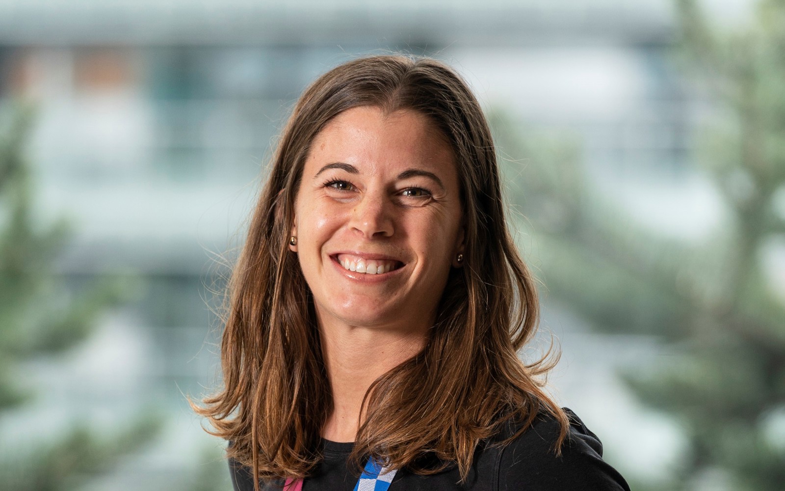 Portrait d'une femme aux longs cheveux bruns vêtue d'un t-shirt noir. Elle porte autour du cou une médaille olympique des Jeux de Tokyo 2020.