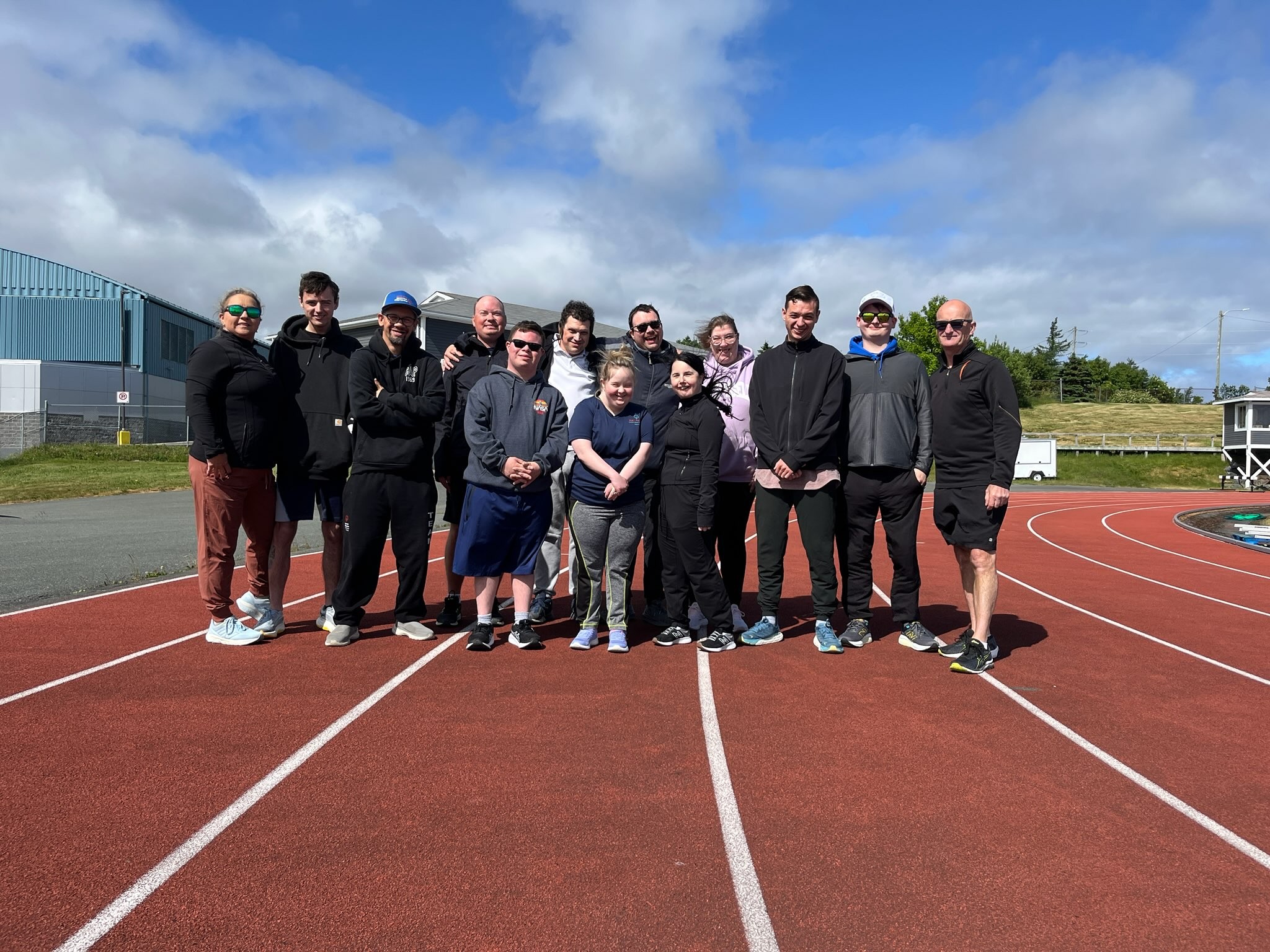 A group photo of a Special Olympics Newfoundland & Labrador team. There is 13 people in the photo and they are all standing on the track.