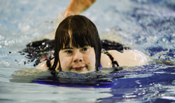 A closeup image of a swimming athlete swimming in a pool. Her head is above the water and she is looking to the right of the camera.
