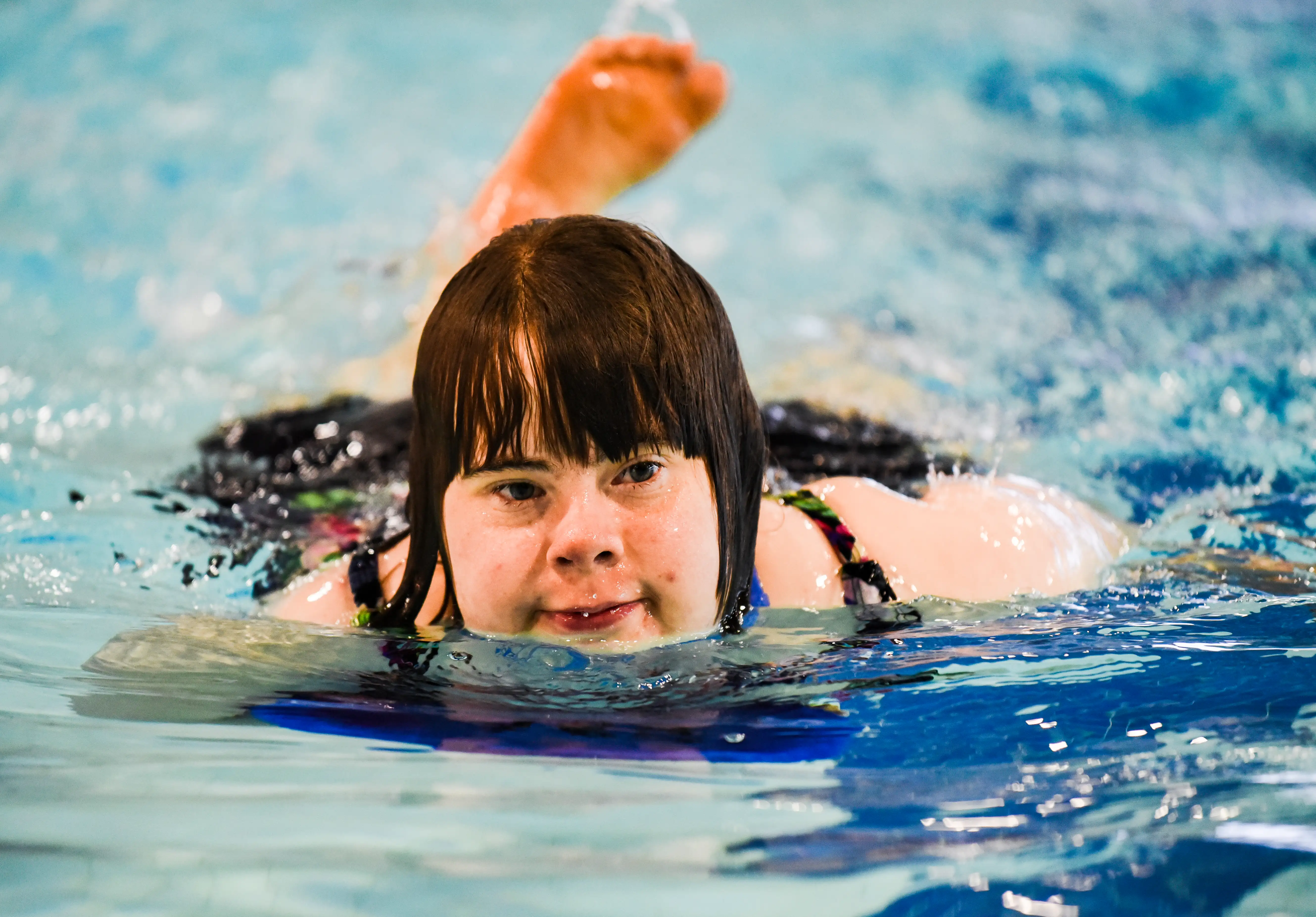 A closeup image of a swimming athlete swimming in a pool. Her head is above the water and she is looking to the right of the camera. A closeup image of a swimming athlete swimming in a pool. Her head is above the water and she is looking to the right of the camera.