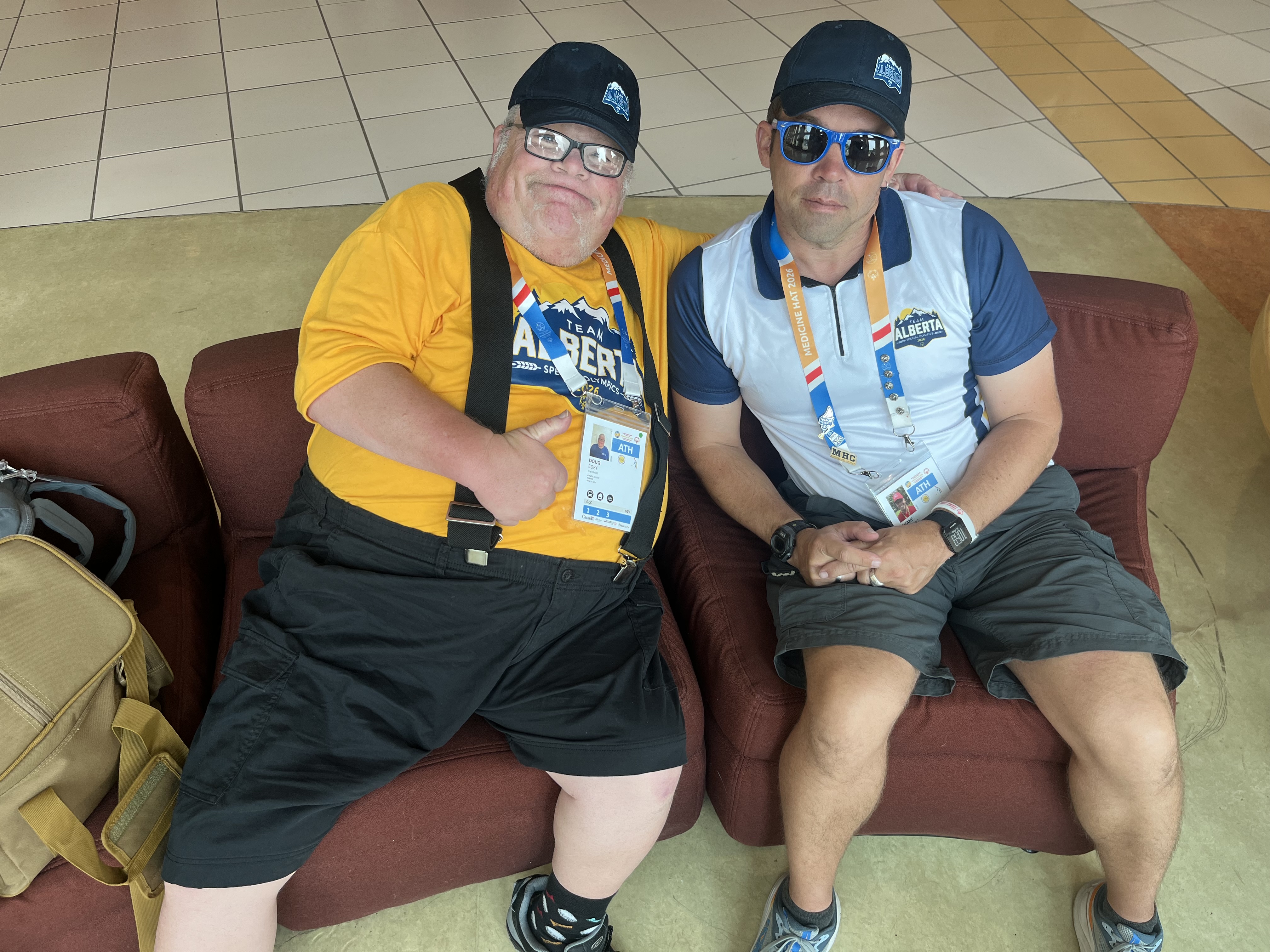 Doug Edey [Left] and Shane Stewart [Right] sitting on a couch together, wearing Special Olympics Alberta apparel. 