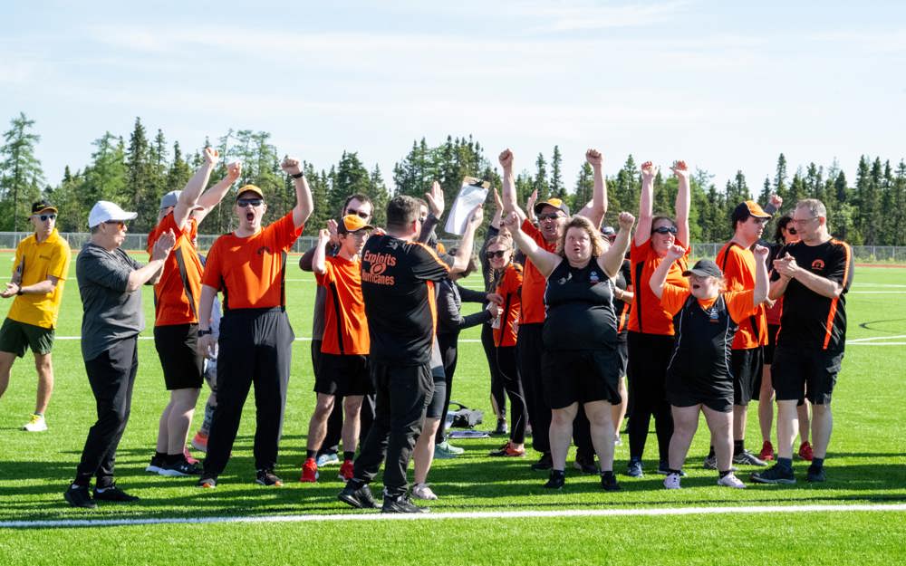 A sports team, out on the field in black and orange jerseys, with their arms up in the air cheering.