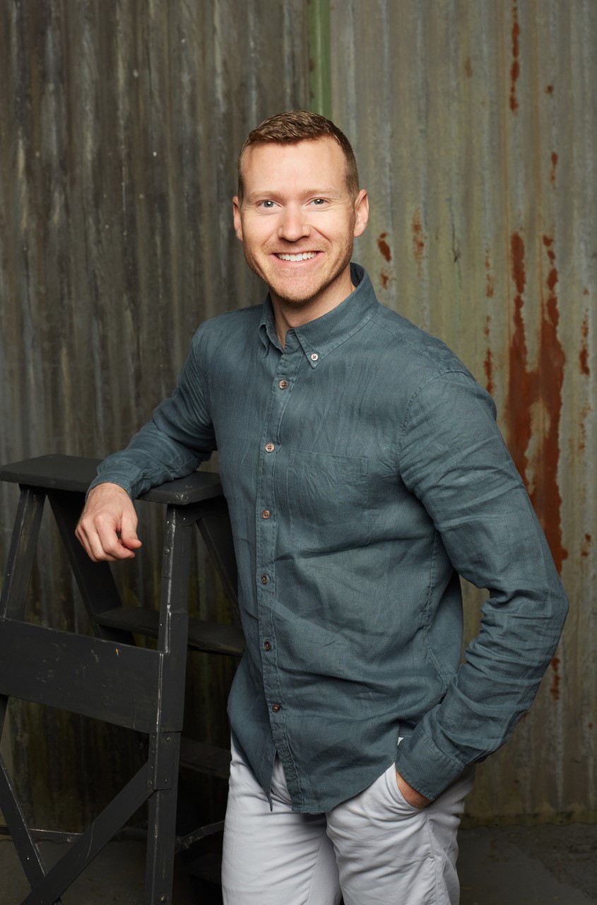 Headshot of a man wearing a grey button up shirt and beige pants. Headshot of a man wearing a grey button up shirt and beige pants.