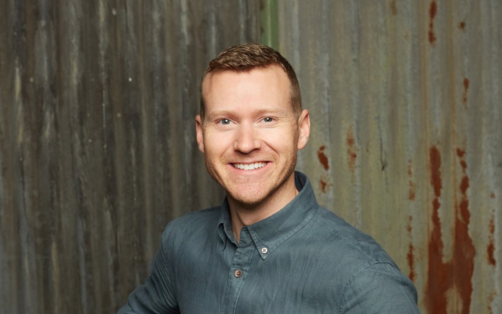 Gros plan sur le visage d'un homme portant une chemise grise boutonnée et un pantalon beige.