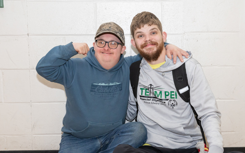 Two Special Olympics athletes sitting by a wall, smiling 