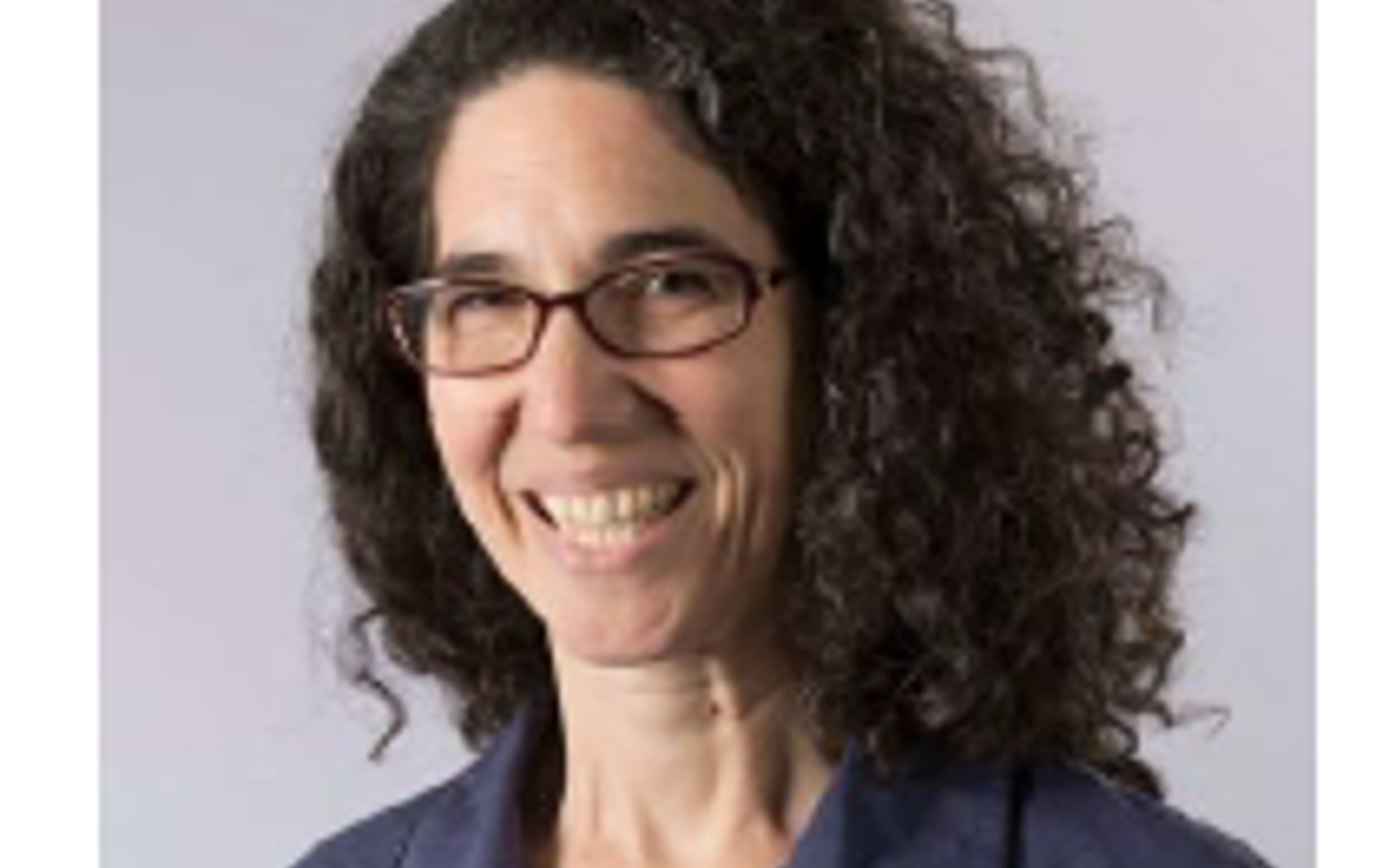 Women with long dark curly hair and glasses wearing a blue button down shirt. 