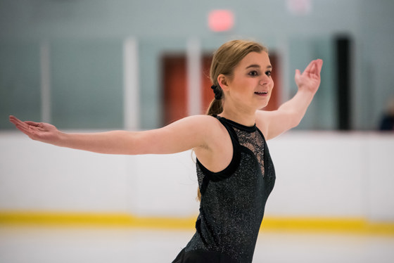 Special Oylmpics BC figure skating athlete finishes her performance with her arms outstretched and a satisfied smile on her face.