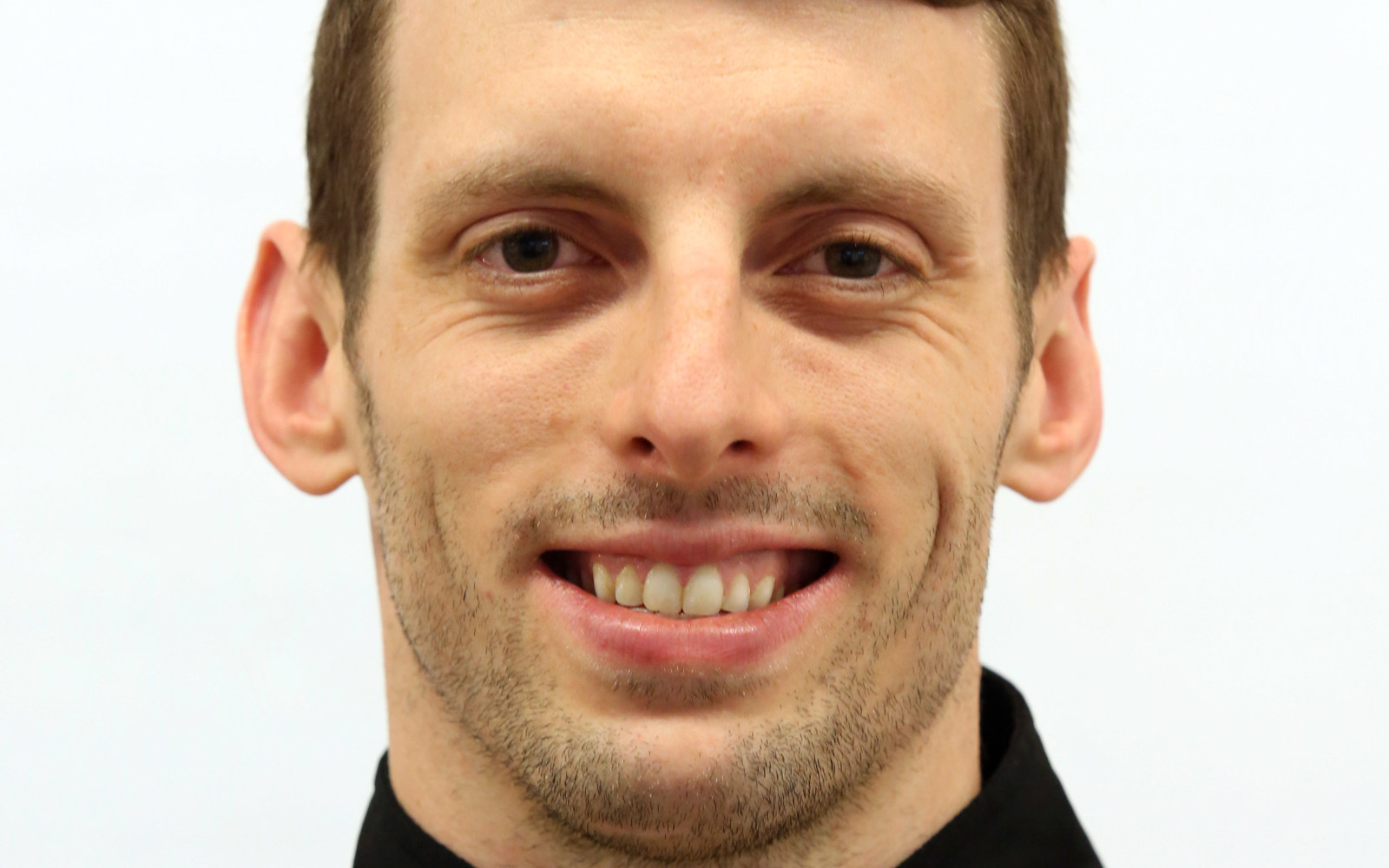 Gros plan sur le visage d'un homme vêtu d'une veste zippée noire.