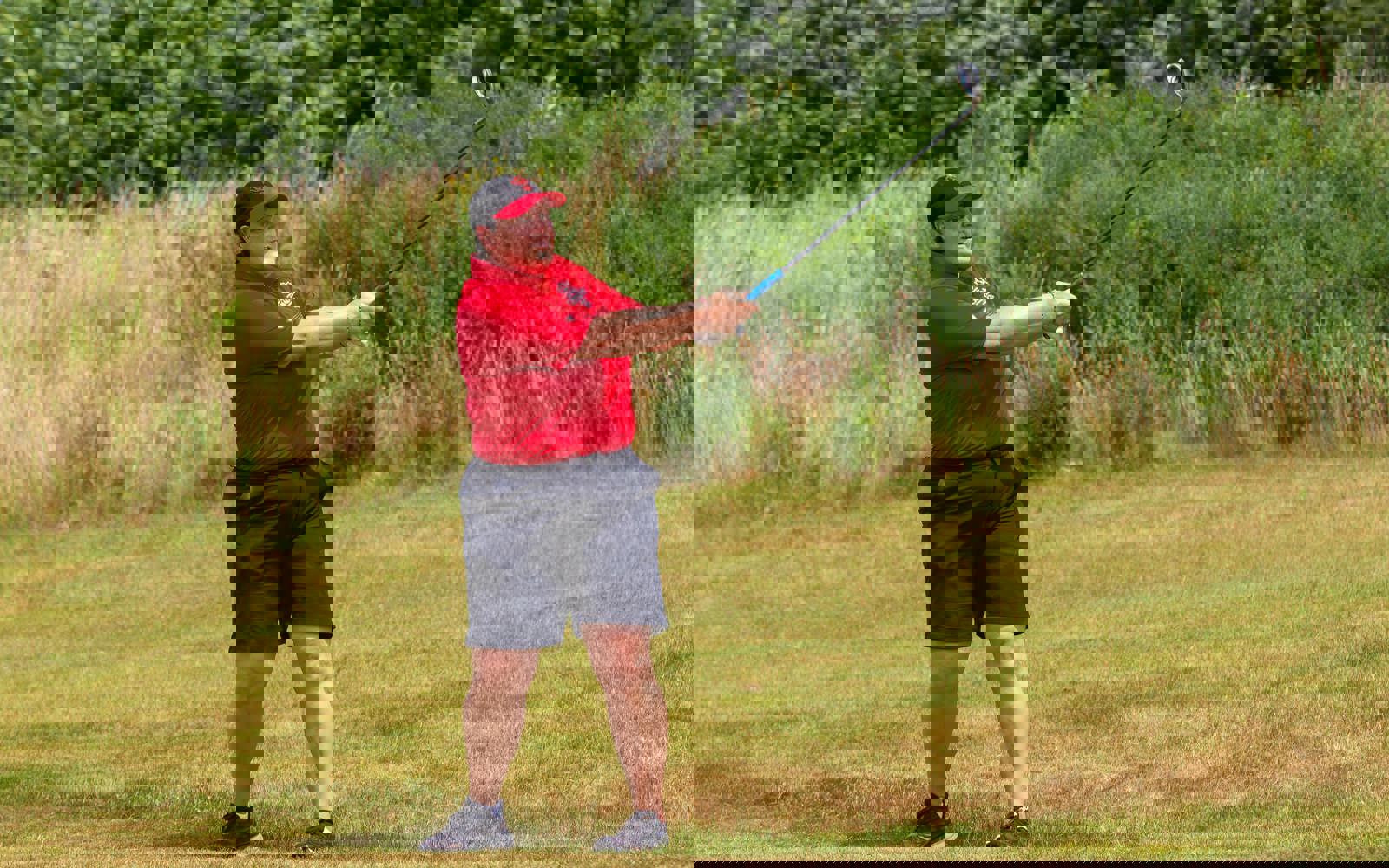 Personne effectuant un swing de golf, vêtue d'un polo rouge, d'une casquette rouge et d'un short noir.